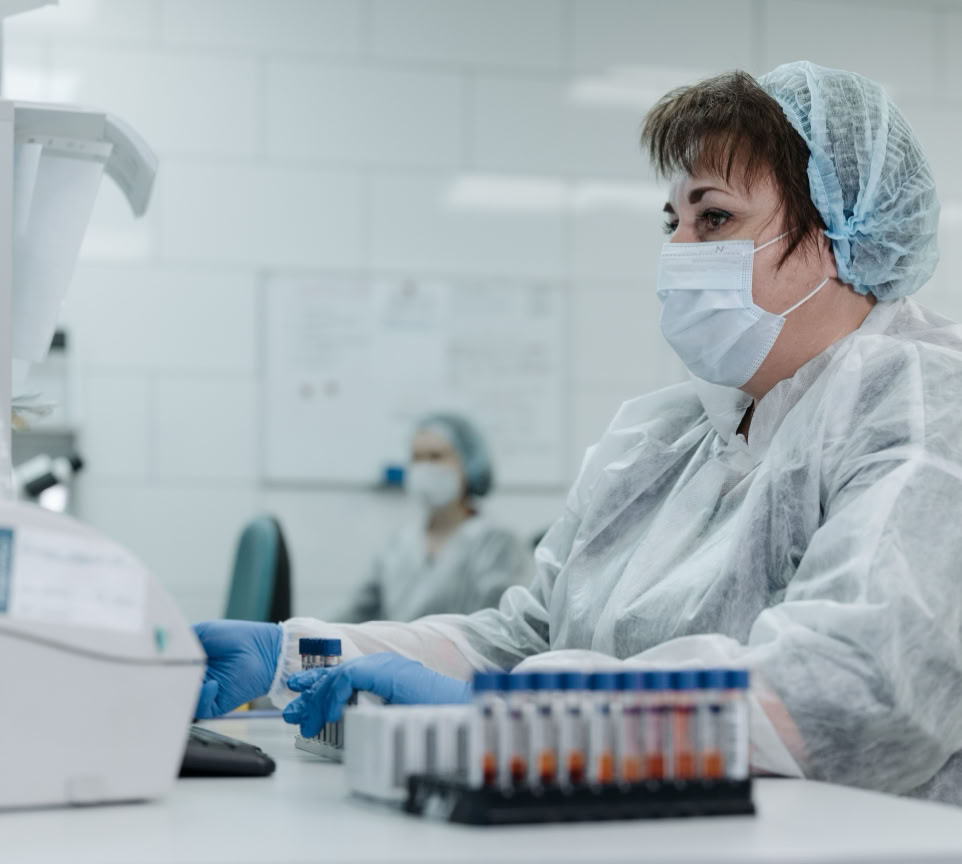 Scientist in protective gear working with lab equipment and samples in a laboratory setting.